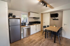 Eine kleine Küche mit Kühlschrank, Mikrowelle, Herd und Spüle. Ein Esstisch mit Stühlen und eine kleine Pflanze sind ebenfalls vorhanden.
