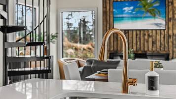 A modern kitchen with a gold faucet, a white dish soap bottle, and a wooden wall with a TV displaying a beach scene.