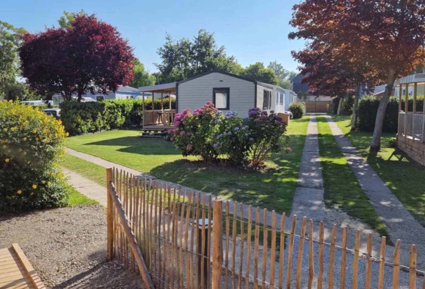 A mobile home with a fenced yard, surrounded by greenery and trees.