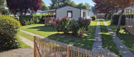 A mobile home with a fenced yard, surrounded by greenery and trees.