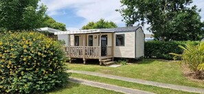 A single-story mobile home with a porch, surrounded by greenery and a pathway. - ZEcamping 3* mobil-home TV BBQ 27m2 4 pers (Pordic)