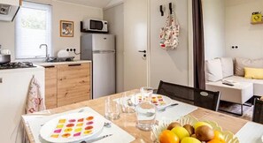A compact kitchen with a microwave, refrigerator, and a dining area with a table set for two. - ZEcamping 3* mobil-home TV BBQ 27m2 4 pers (Pordic)