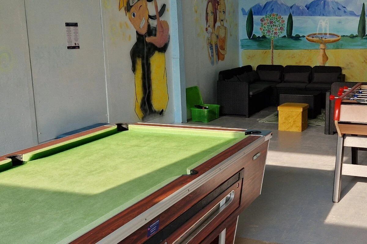 A pool table in a room with a mural, a sofa, and a foosball table.
