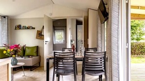 A modern living room with a sofa, a dining table with chairs, and a TV mounted on the wall. - ZEcamping 3 étoiles mobil-home TV LV BBQ 27m2 4 pers (Pordic)
