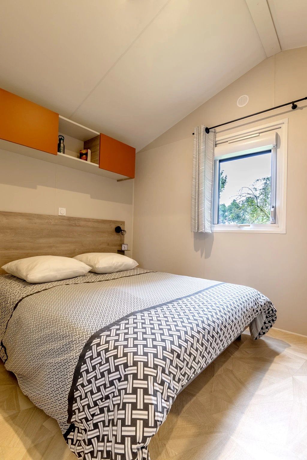 Une chambre à coucher avec un lit, une fenêtre avec des rideaux, une étagère avec des objets et une horloge murale.