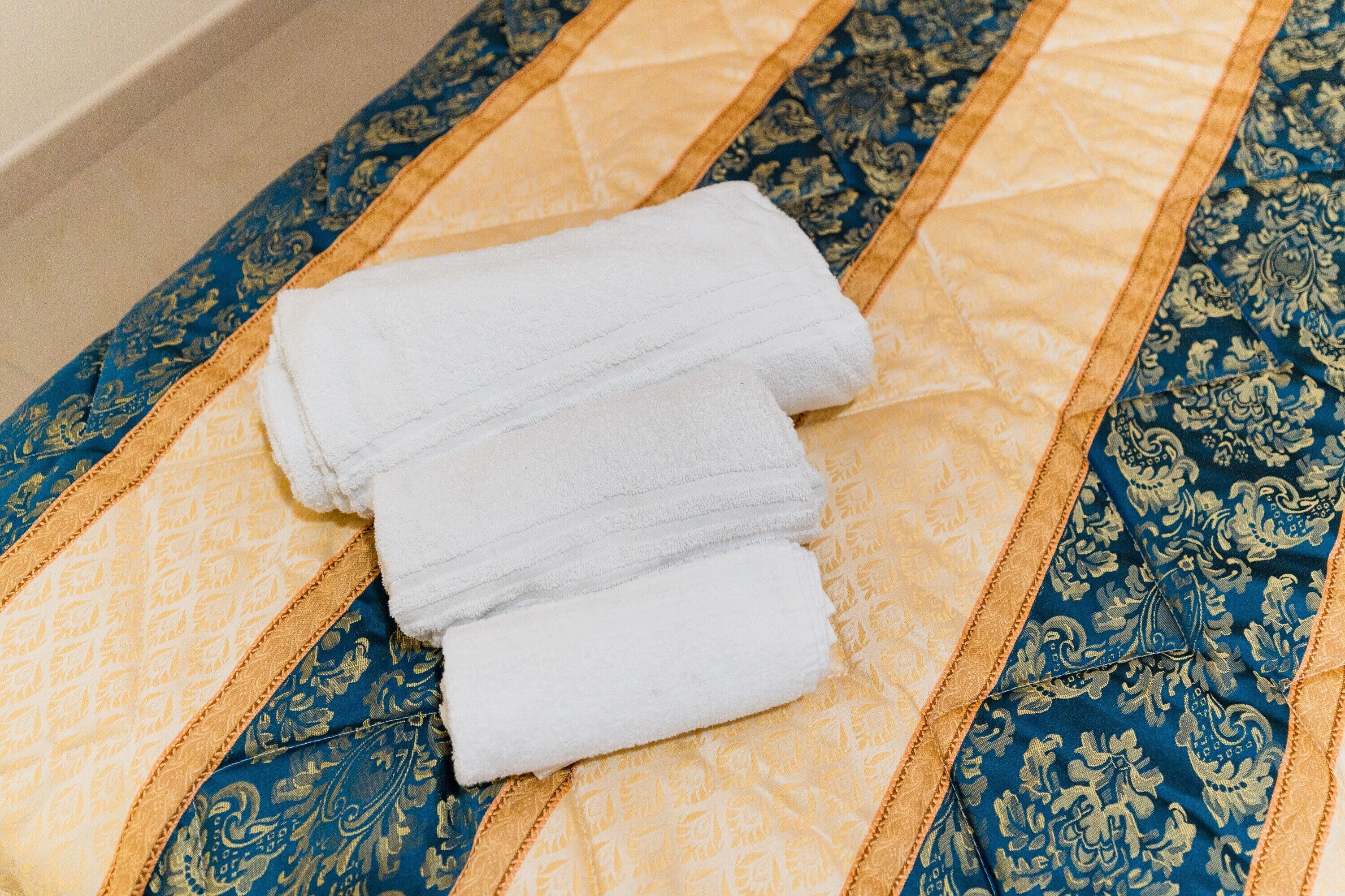Un lit recouvert d’une courtepointe aux motifs bleus et dorés, avec une serviette blanche à proximité.
