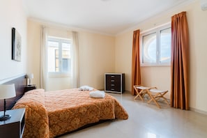 Une chambre d’hôtel comprenant un lit, un bureau, une chaise, une armoire et une fenêtre avec des rideaux.