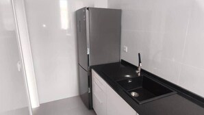 A compact kitchen with a stainless steel refrigerator, a black countertop, and a sink. - Jupiter, apartment in historic building in San Roque neighborhood (Seville)