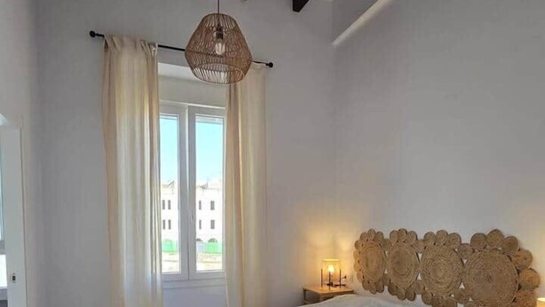 Un dormitorio con una cama grande, un cabecero de madera, una lámpara colgante y una ventana con cortinas.