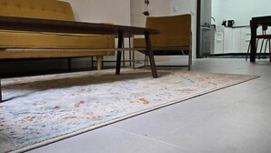 Una habitación con un banco, un tapete y una zona de cocina al fondo.