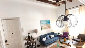 Una sala de estar moderna con un sofá azul, una mesa de comedor de madera preparada para dos personas y una mesa de centro.