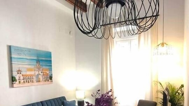 Un comedor con una mesa de madera dispuesta para cuatro personas, un sofá azul y una araña.