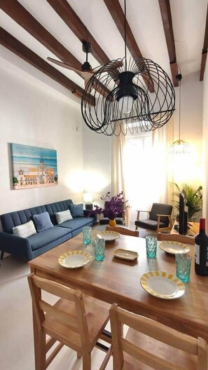 A dining area with a wooden table set for four, a blue sofa, and a chandelier. - Lope (Pinillos), apartment in historic building in San Roque neighborhood. (Seville)