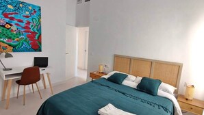 Un dormitorio con una cama, un escritorio, una silla y un cuadro de colores en la pared.