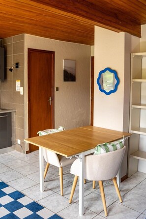 A dining area with a wooden table and two chairs, a blue and white checkered rug, and a wooden ceiling. - ZEcamping 4* animé piscine couverte animaux acceptés locatif TV LV (Granges-sur-Vologne)
