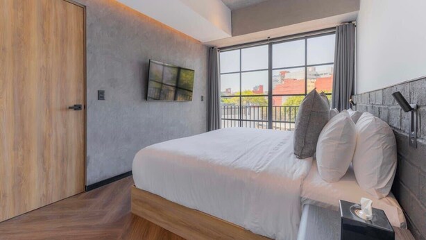 A modern hotel room with a large bed, a TV mounted on the wall, and a window with a view of buildings. - Michoacan Space Lovely Apartment With Balcony (Mexico City)