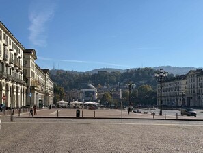 A cobblestone square with historic buildings, a central monument, and a clear view of a hill in the background. - Loft Portici in Torino (Turin)