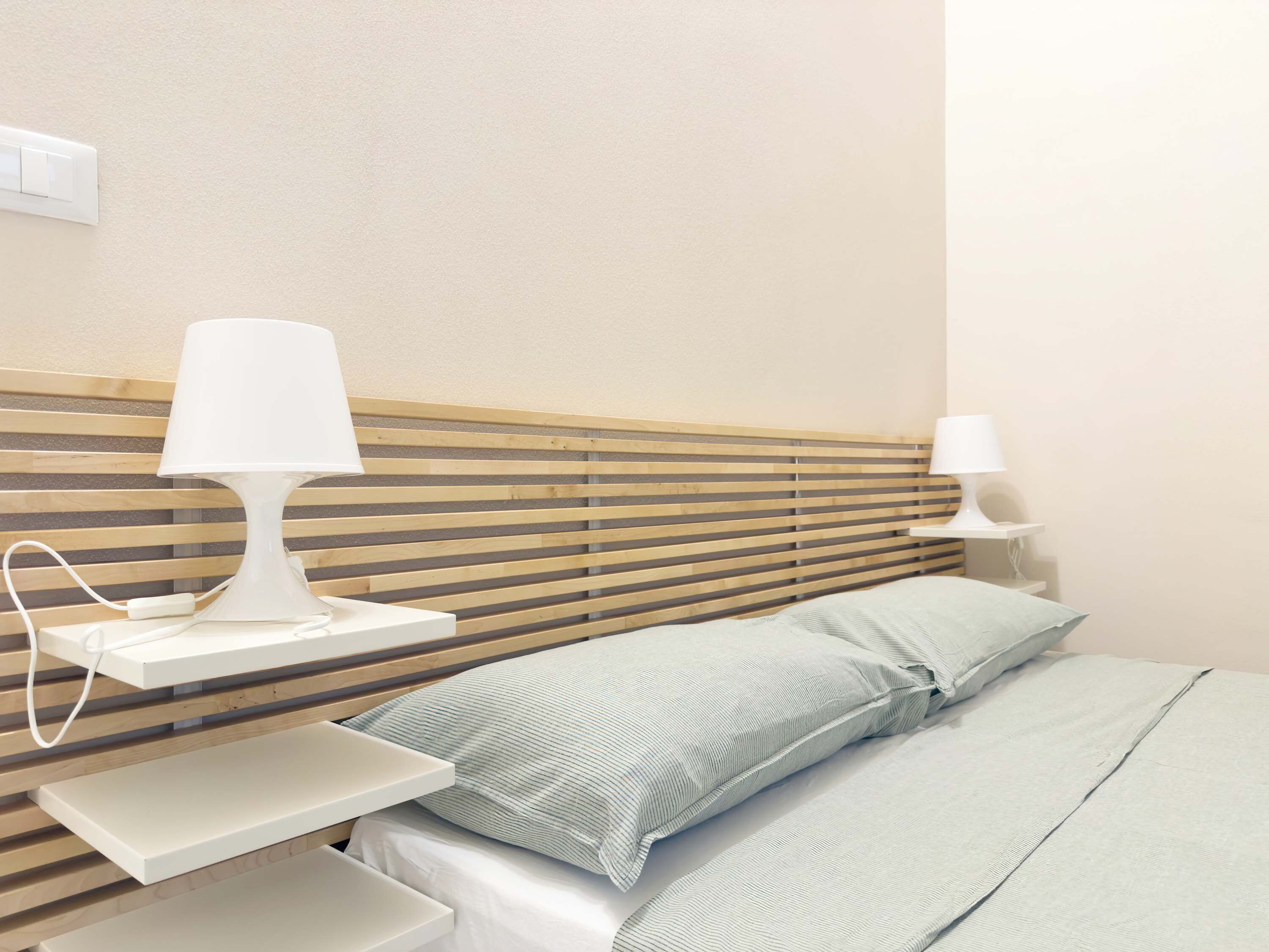 A neatly arranged hotel room with a wooden headboard, a bedside table with a lamp, and a bed with pillows.