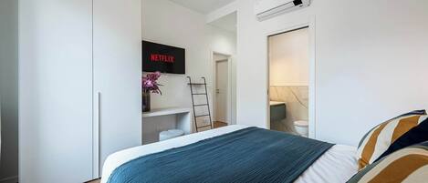 A bedroom with a bed, a TV mounted on the wall, a wardrobe, and a ladder.