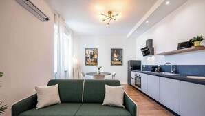 A modern living room with a green sofa, a dining table with chairs, and a kitchen with a sink and stove. - Casa Belfiore in Firenze (Florence)