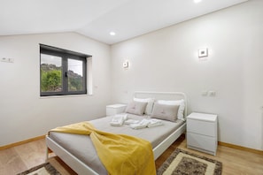 Un dormitorio con cama, mesitas de noche, una ventana y vistas al exterior.