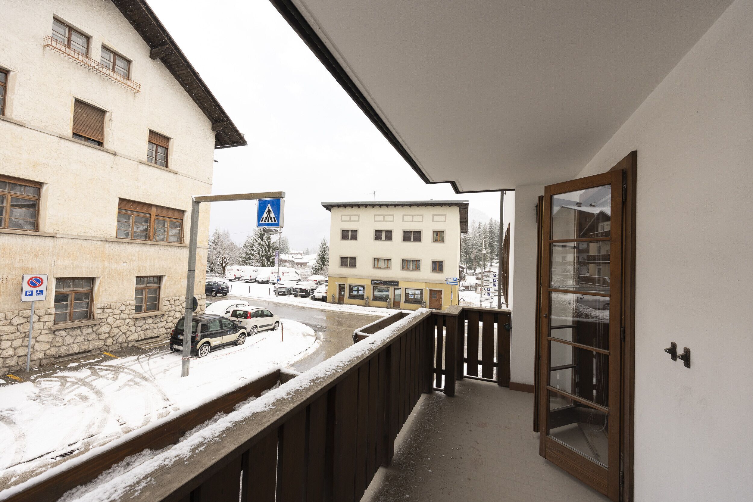 A balcony with a view of a street, a building with a sign, and a snow-covered ground.