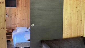 Una cabana de fusta amb dos llits, una televisió i un sofà.