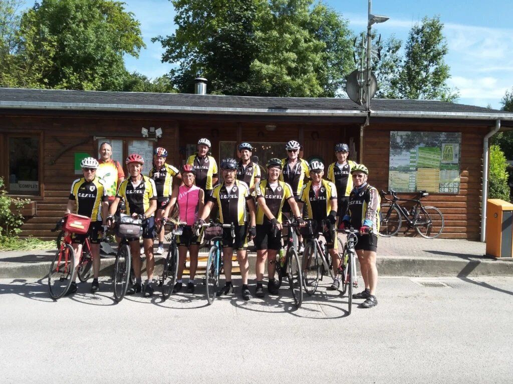 A group of cyclists in front of a wooden building with a sign that reads "COMPLEX".