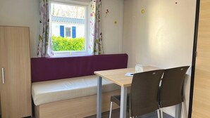 A small room with a wooden wardrobe, a purple bench, a wooden table, and two chairs. - ZEcamping 2* chiens acceptés locatif TV clim 20m2 2 pers (Angicourt)