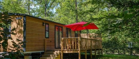 A wooden cabin with a covered deck and a red umbrella.