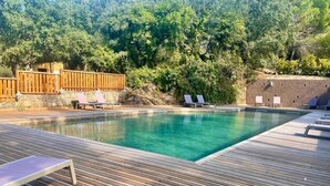 Ein rechteckiger Pool mit einer Holzterrasse, umgeben von Liegestühlen und einem Holzzaun.