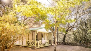 Eine kleine, eingeschossige Holzhütte mit Veranda, umgeben von Bäumen.