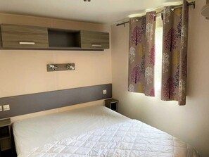 A hotel room with a bed, a bedside table, a wall-mounted shelf, and a curtain with a tree pattern. - ZEcamping 3 étoiles piscine locatif clim 35m2 6 pers (Sartène)