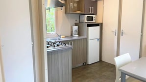 A compact kitchen with a gas stove, microwave, coffee maker, and refrigerator. - ZEcamping 3 étoiles piscine locatif clim 35m2 6 pers (Sartène)