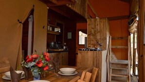 Ein rustikaler Essbereich mit Holztisch, gedeckt für zwei Personen, einer Vase mit roten Blumen und einer Küchenzeile mit Holzschränken und Spüle.