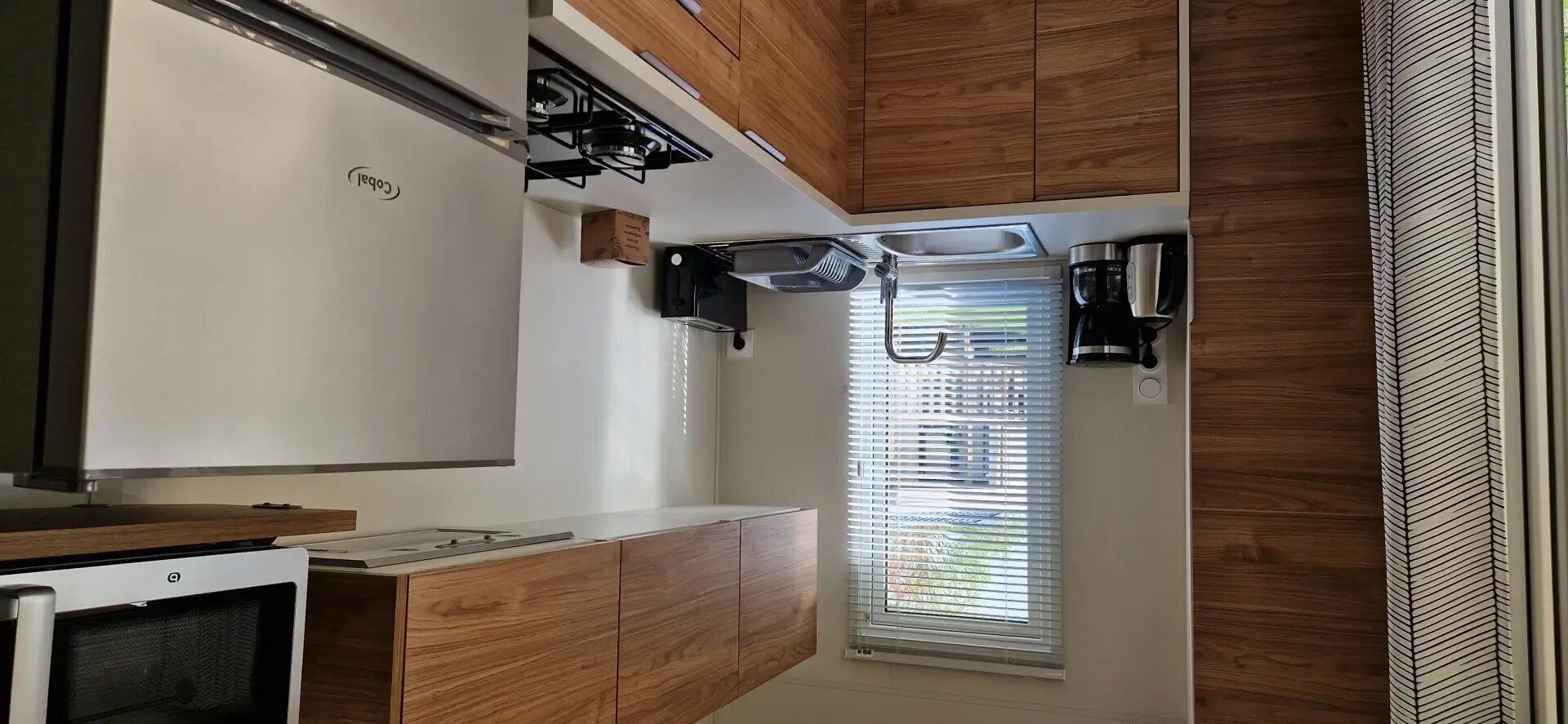 A compact kitchen with a built-in oven, a coffee machine, and a window with blinds.