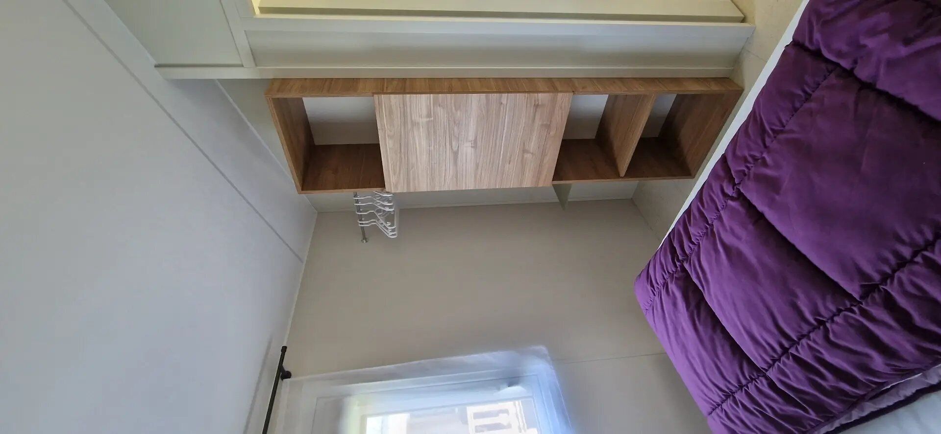 Een kamer met een houten plank, een paars bed en een witte deur.