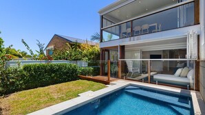 Una casa moderna de dos pisos con un patio cubierto de cristal y una piscina.
