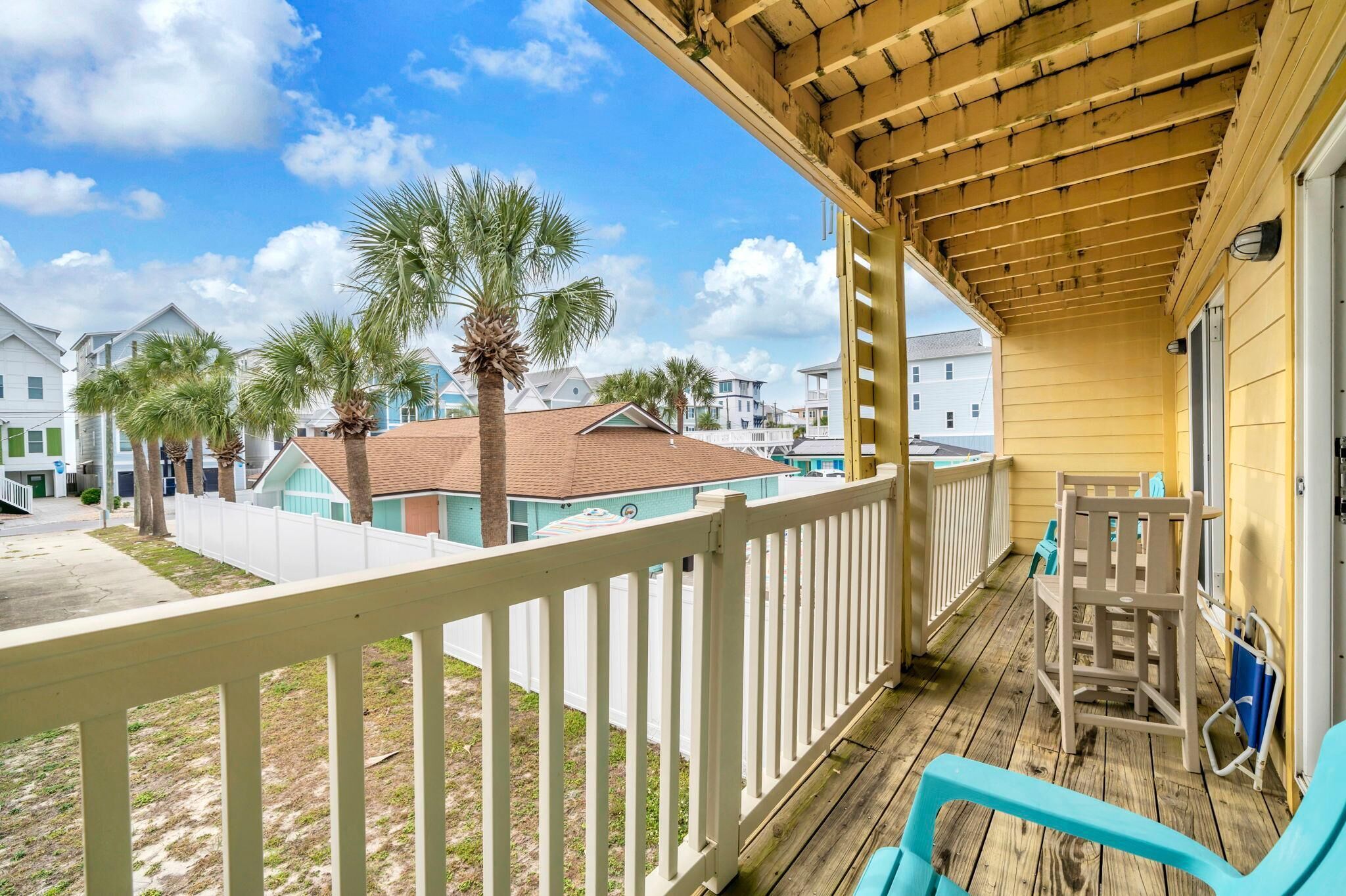 A wooden deck with a white railing, a covered porch, and a view of neighboring houses and palm trees.