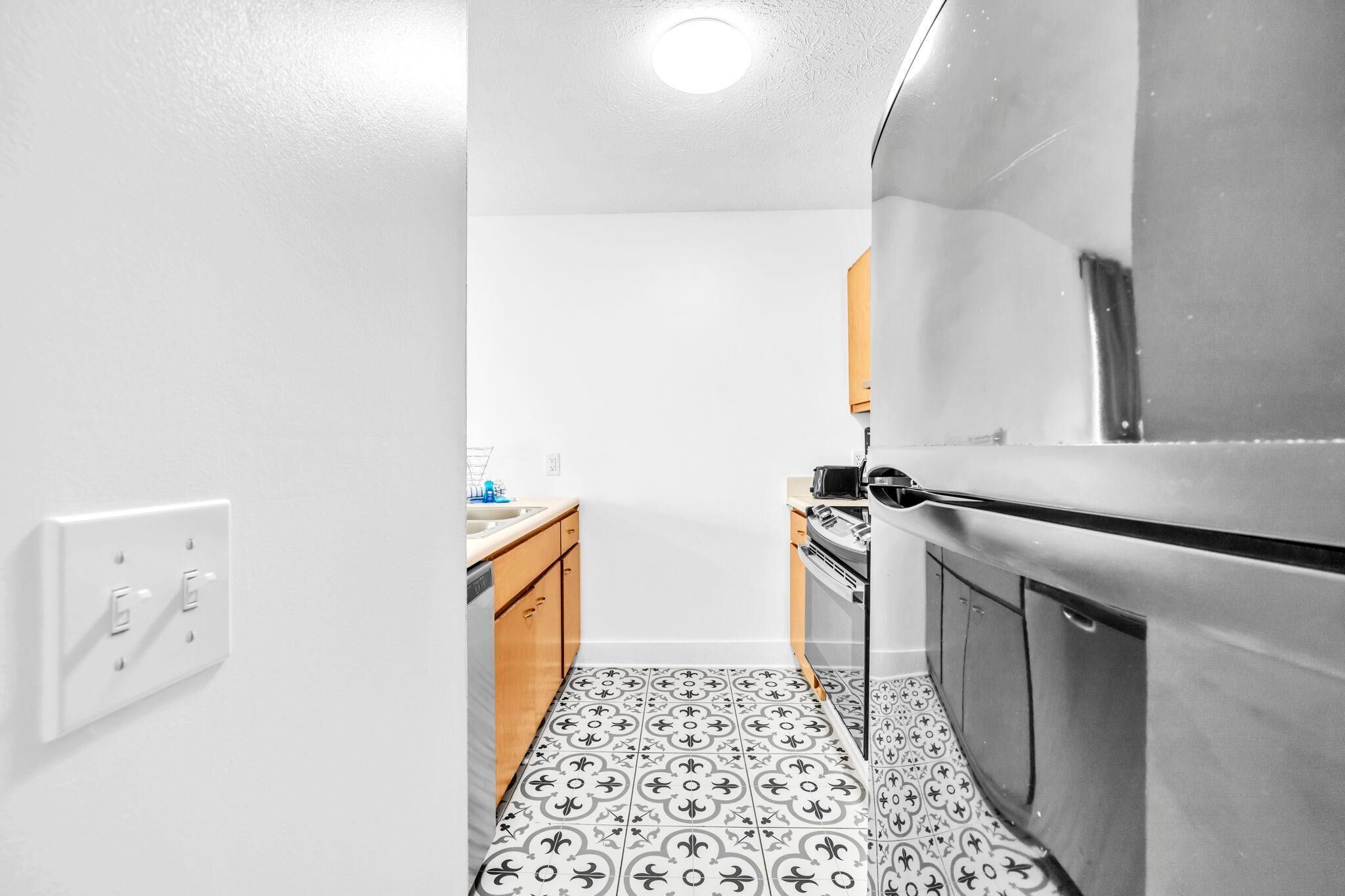 A compact kitchen with white walls, a patterned floor, and modern appliances including a refrigerator and stove.
