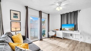 En moderne stue med en grå sofa, et hvidt skrivebord og et stort fjernsyn.