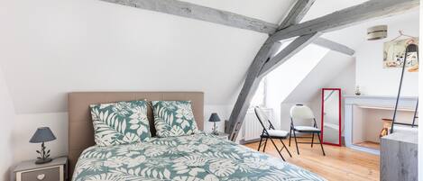 Un dormitorio con cama, mesita de noche, una silla y un escritorio con otra silla.