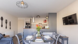 A dining area with a round table, chairs, a vase with flowers, and a television mounted on the wall. - Gîte à l'aube – 3 bedrooms (Saint-Aignan)