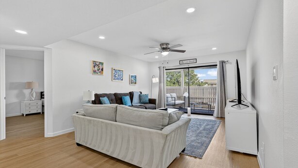 Un salon moderne avec un canapé, un ventilateur de plafond et une vue sur l’extérieur grâce à une porte vitrée.