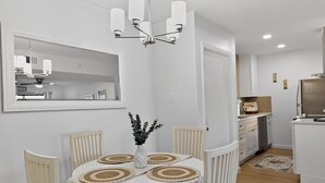 Un coin repas avec une table blanche, quatre chaises, un vase avec des plantes et un lustre.