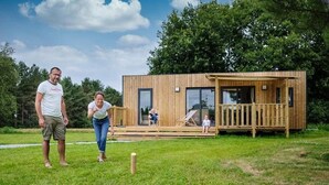 A wooden cabin with a deck, a grassy yard, and a person playing croquet. - ZEcamping 4* espace bien-être avec jacuzzi et sauna cadre verdoyant (Caro)