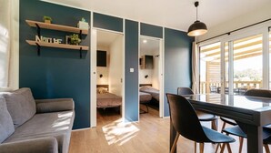 A modern living space with a sofa, a dining table with chairs, a kitchen area, and a bedroom with a bed. - ZEcamping 4* espace bien-être avec jacuzzi et sauna cadre verdoyant (Caro)