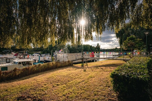 A riverside park with boats docked, a wooden bridge, and trees. - ZEcamping 3 étoiles à proximité de Paris et de Disneyland (Neuilly-sur-Marne)