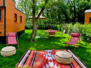 Une maison en bois dotée d’un patio comprenant une table et quatre chaises, le tout entouré d’une végétation luxuriante.