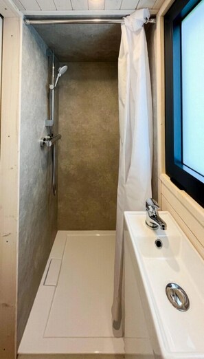 Une petite salle de bain fermée, équipée d’une douche, d’un lavabo et d’une fenêtre.